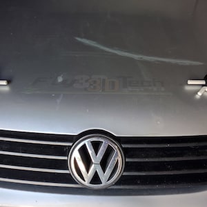 以下が含まれることがあります： 黒いグリルとフードの両側に白いプラスチックフックが付いたシルバーのフォルクスワーゲン