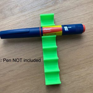 May include: Green plastic pen holder with five slots. The holder is designed to hold insulin pens. The holder is on a wooden surface. NOTE: Pen NOT included.