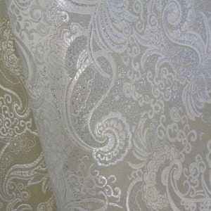 Könnte beinhalten: Weißer Stoff mit einem silbernen Glitzer-Paisley-Muster.