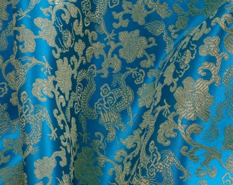 May include: A close-up of a blue fabric with a gold embroidered pattern of stylized flowers and birds. The fabric has a silky sheen and a luxurious feel.