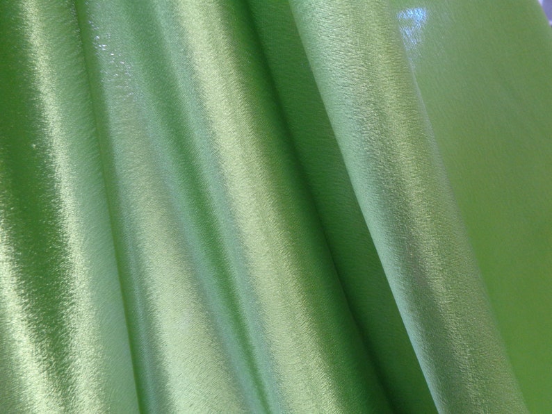 May include: A close-up of a green fabric with a subtle shimmer. The fabric is folded and draped, showing its texture and drape.