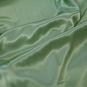 May include: A smooth, green satin fabric with soft folds and wrinkles. The fabric has a subtle sheen and a luxurious feel.