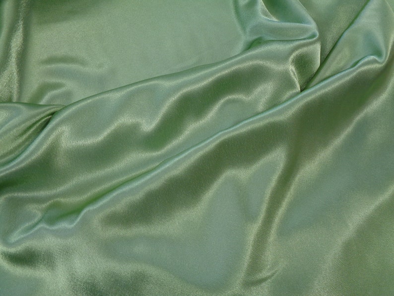May include: A smooth, green satin fabric with soft folds and wrinkles. The fabric has a subtle sheen and a luxurious feel.