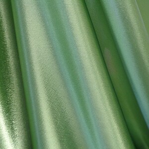 May include: Close-up of a smooth, green fabric with a subtle sheen. The fabric is folded and draped, creating soft, flowing lines.
