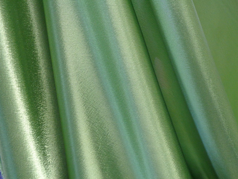 May include: Close-up of a smooth, green fabric with a subtle sheen. The fabric is folded and draped, creating soft, flowing lines.