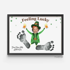 May include: A white framed print with a child's footprint art. The print features a cartoon leprechaun holding two mugs of beer and the text "Feeling Lucky". The text "From Your Little Leprechaun" is also included.