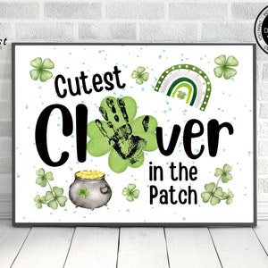 Puede incluir: Un cartel imprimible con el texto "Cutest Clover in the Patch" y una huella de mano en el centro. El cartel está decorado con tréboles verdes, una olla de oro y un arcoíris.