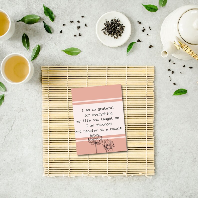 May include: A pink card with a quote about gratitude and happiness. The quote reads: "I am so grateful for everything my life has taught me! I am stronger and happier as a result." The card features a black and white illustration of two lotus flowers.