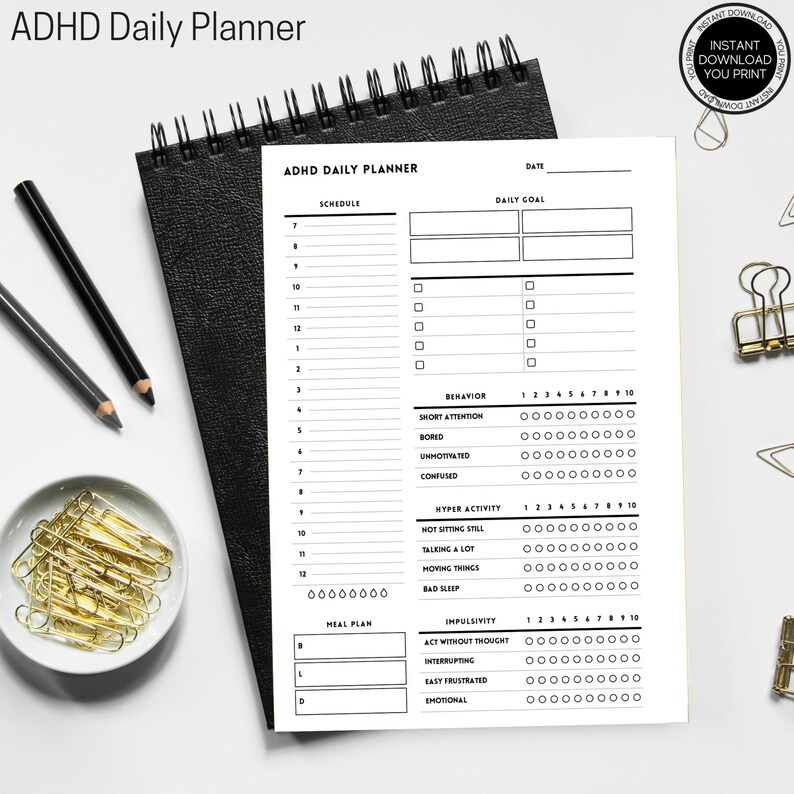 K&ouml;nnte beinhalten: Ein schwarzer, spiralgebundener ADHD-Tagesplaner mit wei&szlig;em Innenraum. Der Planer enth&auml;lt Abschnitte f&uuml;r die Planung, Tagesziele, Essensplanung und Verhaltensverfolgung. Der Text "ADHD Daily Planner" steht oben.