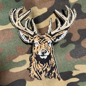 May include: Embroidered patch of a brown and white deer head with large antlers. The deer is looking directly at the viewer.