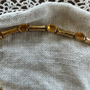 May include: A gold chain necklace with oval-shaped amber gemstones. The necklace is lying on a white fabric surface.