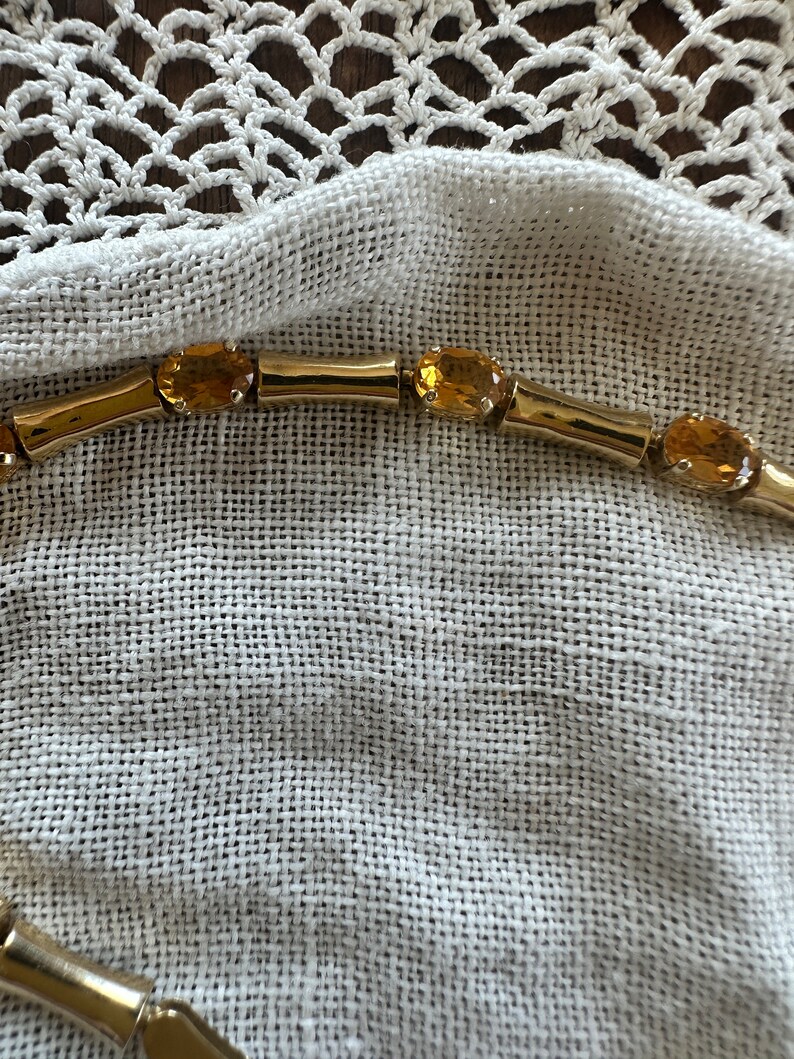 May include: A gold chain necklace with oval-shaped amber gemstones. The necklace is lying on a white fabric surface.