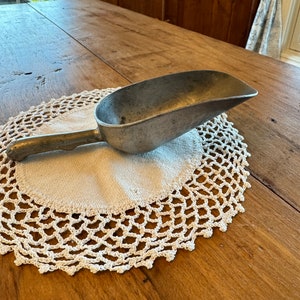 Peut inclure: Une louche en métal argenté avec une poignée, reposant sur un napperon en crochet blanc sur une table en bois.