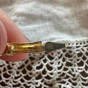 May include: Close-up of a gold-toned bracelet clasp with a diamond-shaped marking that reads "1/20 12K GF".