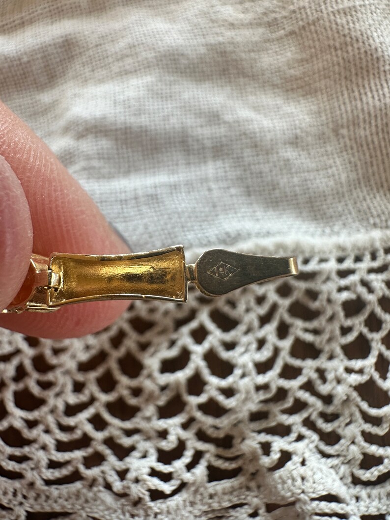 May include: Close-up of a gold-toned bracelet clasp with a diamond-shaped marking that reads "1/20 12K GF".