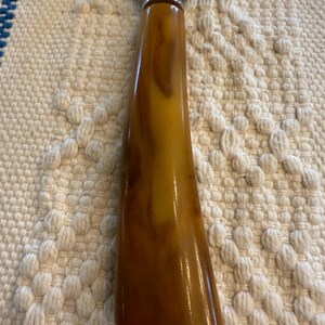May include: Cheese knife with a stainless steel blade and a handle with a marbled amber and brown pattern. The handle has a glossy finish and a silver metal collar where it meets the blade.