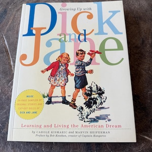May include: A book titled "Dick and Jane" with a colourful illustration of two children and a dog. The cover text includes "Growing Up With" and "Learning and Living the American Dream".