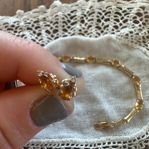 May include: A pair of gold earrings with teardrop-shaped amber stones. The earrings are shown next to a gold bracelet with oval-shaped amber stones.