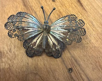 May include: A silver butterfly brooch with detailed filigree wings. The brooch features an openwork design, highlighting the craftsmanship. The butterfly's body and antennae are also silver, creating a beautiful accessory. The brooch is a decorative item.