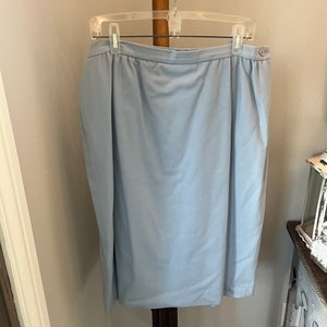 May include: A light blue skirt with a button closure and a waistband. The skirt is hanging on a wooden hanger.