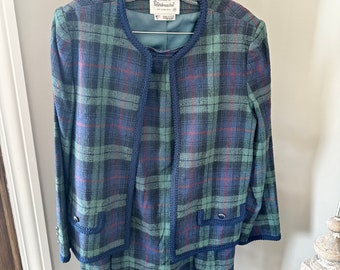 Op de afbeelding: Een groene, blauwe en rode geruite rokpak met een marineblauwe bies. Het jasje heeft een kraag en lange mouwen. De rok is knielengte. Het label luidt "The Clothes by Windbreaker".