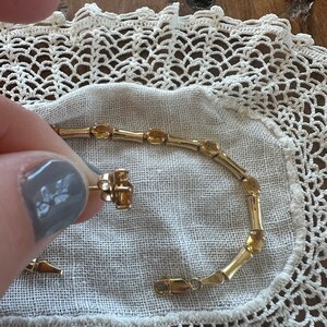 May include: A gold bracelet with oval-shaped amber stones. The bracelet has a clasp closure.