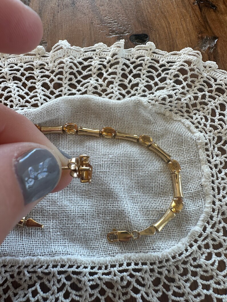 May include: A gold bracelet with oval-shaped amber stones. The bracelet has a clasp closure.