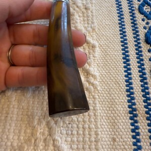 May include: A vintage tool with a dark brown, marbled handle and a silver metal top. The handle has a curved shape and a polished finish. The tool's metal portion is a dull silver color. The background is a cream-colored fabric with blue stripes.