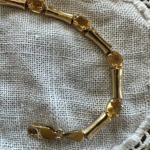 May include: A gold bracelet with a clasp closure and multiple oval-shaped topaz gemstones.