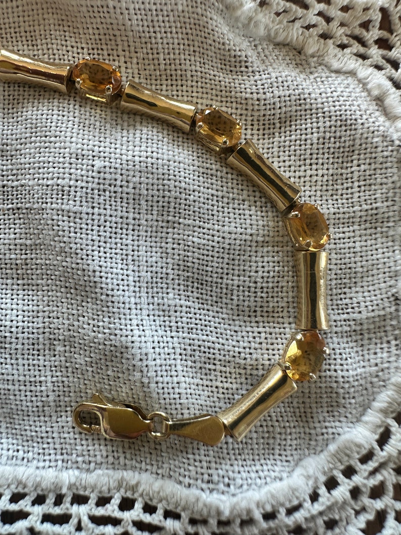 May include: A gold bracelet with a clasp closure and multiple oval-shaped topaz gemstones.