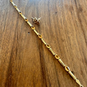 May include: A gold bracelet with a bamboo-style design and oval-shaped orange gemstones. A pair of matching earrings with orange gemstones are also included.