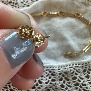 May include: Close-up of a pair of gold earrings with a flower-shaped design. The earrings are marked "14K" on the back.