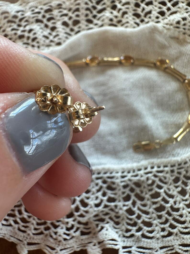 May include: Close-up of a pair of gold earrings with a flower-shaped design. The earrings are marked "14K" on the back.