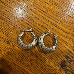 May include: A pair of silver hoop earrings with a detailed floral design.