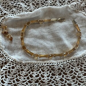 May include: A gold necklace with amber stones and matching earrings. The necklace is on a white crocheted doily.