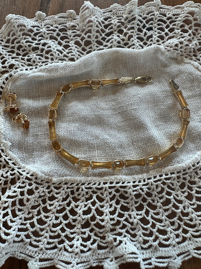 May include: A gold necklace with amber stones and matching earrings. The necklace is on a white crocheted doily.