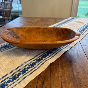 May include: A wooden oval serving bowl with a natural wood finish. The bowl is sitting on a white and blue striped table runner.