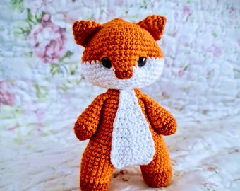 May include: A handmade crochet fox toy. The fox is primarily orange with a white face and chest. It has small, pointed ears and black eyes. The toy is standing upright and appears to be made of soft yarn.
