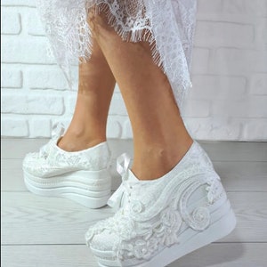 May include: White lace wedding sneakers with a platform sole. The sneakers have a delicate lace design and are perfect for a bride who wants to be comfortable on her wedding day.
