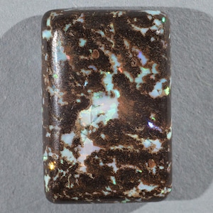 Peut inclure: Un cabochon d'opale rectangulaire brun et blanc. L'opale a une matrice brun foncé avec des reflets blancs et bleus.