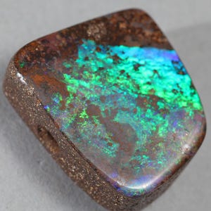 Può includere: Un cabochon di opale verde e blu con una matrice marrone. L'opale è incastonato in una montatura in pietra naturale grezza.