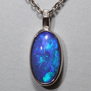 Op de afbeelding: Een zilveren ketting met een hanger met een blauwe opaal edelsteen in een zilveren ovale lijst.