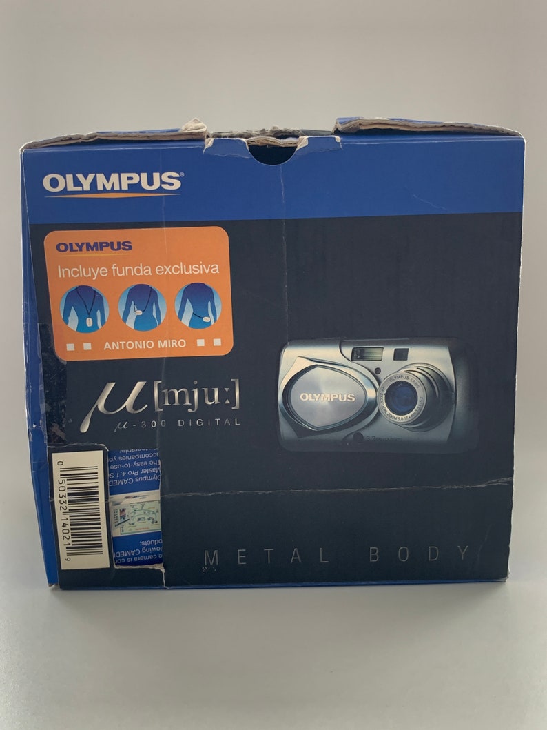 May include: A blue box with a silver Olympus M[mju:] digital camera on the front. The box has the text "Olympus" and "M[mju:] 300 Digital" on it. The camera has a silver metal body and a black lens.