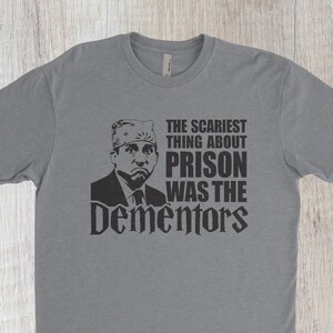 May include: A gray t-shirt with a black and white image of a man wearing a hat. The text on the shirt reads "The scariest thing about prison was the Dementors."