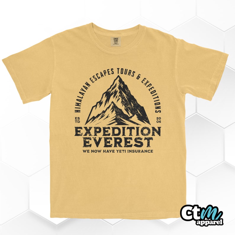 Op de afbeelding: Mosterdgeel t-shirt met een zwarte, verweerde afbeelding. De afbeelding toont een bergsilhouette met de tekst "Himalayan Escapes Tours & Expeditions" en "Expedition Everest". Het shirt bevat ook de tekst "We Now Have Yeti Insurance".