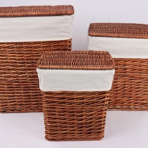 May include: Three brown wicker storage baskets with matching lids and white fabric liners. The baskets are rectangular and vary in size, suitable for laundry or general storage. The lids are hinged and the baskets are woven.