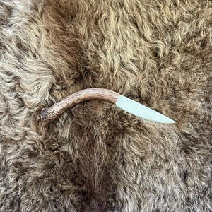 May include: A small, handmade knife with a brown antler handle and a light blue blade. The knife is lying on a brown fur surface.