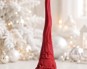 May include: A tall, red, tapered candle shaped like a gnome with a long, pointed hat. The gnome features a detailed beard, mustache, and facial features. It holds a rectangular sign with the embossed text Merry Christmas in red wax.