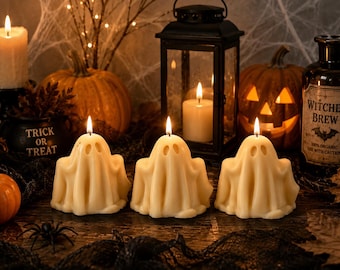 Könnte beinhalten: Drei cremeweiße, geisterförmige Kerzen mit brennenden Dochten, jede mit zwei hohlen Augenhöhlen. Die Kerzen sind in einer Reihe angeordnet und von Halloween-Dekorationen wie Kürbissen, einer schwarzen Laterne und einer Flasche umgeben.