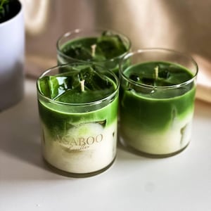 May include: Three green and white scented candles in glass jars with the text "AGABOO Candles" on the front of one jar.